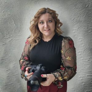 Professional female photographer in a stylish outfit, confidently holding a Canon camera with a long lens, set against a textured background.